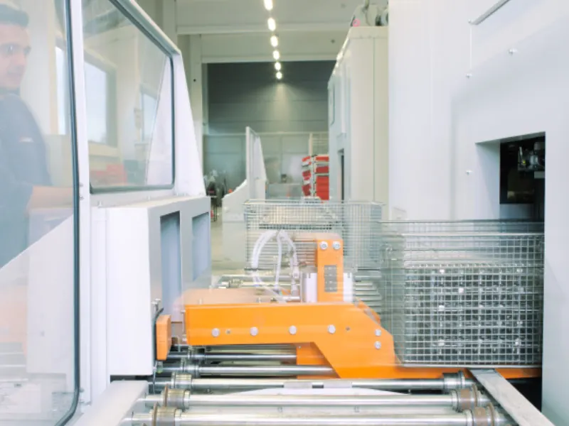 Warenkörbe mit Bauteilen auf der Zuführung einer Industriewaschanlage